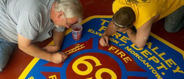 Two men painting the Twin Valley Fire Department logo on the floor of the firehouse