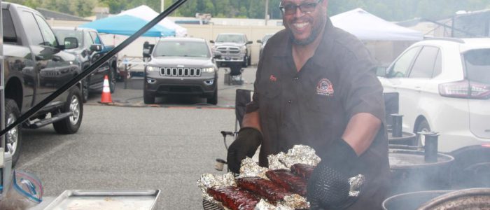 A man smiling while holding a tray of cooked meat